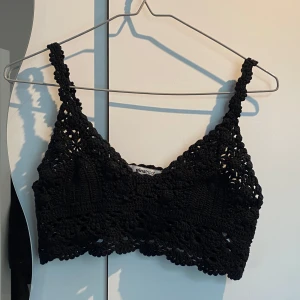 Svart virkad topp från Gina Tricot - Superfin svart virkad topp från Gina Tricot med breda axelband och snyggt mönstrad spetsdetalj. Perfekt till sommaren och enkel att styla med både jeans och kjol. Toppen är ärmlös och har en croppad passform.