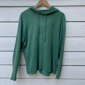 Grön hoodie från Ralph Lauren - Säljer en grön hoodie från Ralph Lauren med dragsko i huvan och lång ärm. Tröjan har en liten broderad logga på bröstet och är gjord i mjuk bomull. Perfekt för chill dagar eller när du vill ha en avslappnad stil.