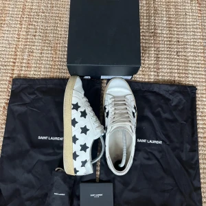 Saint Laurent skor - Snygga vita sneakers från Saint Laurent med svarta stjärnor. De är lite creasade där fram men annars fint skick. De är i storlek 42 men skulle säga att de även passar 43. Extra snören medföljer och de två orginal skopåsarna och skolådan. Hör av för eventuella frågor.