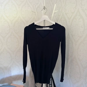 Svart v-ringad tröja från Zara - Snygg svart långärmad tröja från Zara med v-ringning. Tröjan är i en slim passform och tillverkad av mjukt material med rayon, nylon och elastan som ger en skön stretch. Perfekt att styla med jeans eller kjol för en clean look.