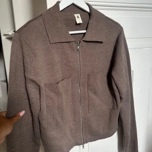 Brun stickad overshirt från Åhléns XS - Säljer en brun stickad overshirt från Åhléns i storlek XS. Jackan har två stora fickor framtill, dragkedja och klassisk krage. Perfekt för lager-på-lager och chill vibes. Enkel och stilren design som funkar till det mesta.