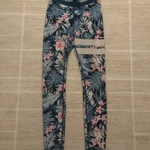 Blommiga leggings från Stronger XS - Tränings tights från Stronger i storlek XS med blommönster i blått, rosa och vitt. Hög midja med logga, stretchigt material. Perfekta för träning. 