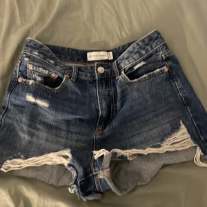 Blå jeansshorts från Stradivarius - Snygga blå jeansshorts från Stradivarius med hög midja och fransade kanter. De har slitna detaljer framtill och klassiska fickor både fram och bak. Perfekta för sommarens alla äventyr och har en loose passform för chill vibe.