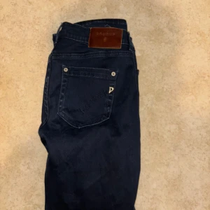 Mörkblå jeans från Dondup, stl 30 - Säljer ett par mörkblå jeans från Dondup i klassisk femficksmodell. Jeansen har raka ben, snygga detaljer med metallnitar och läderpatch bak i midjan. Materialet är jeans och passformen är normal. Perfekta för dig som gillar stilrena och tidlösa byxor. Pris kan sänkas vid snabb affär.