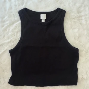 Svart croppad linnetopp från H&M - En svart, croppad linnetopp från H&M i mjuk bomull. Toppen är ärmlös med breda axelband och rund halsringning. Perfekt att matcha med jeans eller kjol för en enkel och stilren look.