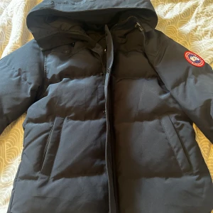 Marinblå dunjacka från Canada Goose passar Strl S - Säljer en marinblå dunjacka från Canada Goose med klassisk patch på ärmen. Använd några enstaka gånger under förra vintern, säljer pågrund av att jag växt ur den. Jackan har huva, dragkedja och stora fickor framtill. Perfekt för kalla dagar och riktigt snygg streetstil. Fodrad insida och rejäla axelband för att bära jackan som ryggsäck. Pris kan diskuteras vid snabb och smidig affär.
