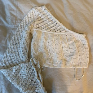 Vit stickad oneshoulder topp - Säljer en superfin vit stickad topp med oneshoulder-design och lång ärm. Toppen har ett luftigt, virkat mönster och croppad passform. Perfekt för dig som vill sticka ut med en unik och trendig look. köpt för 400kr