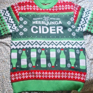 Herrljunga Cider jultröja i grönt och rött - Unik jultröja med Herrljunga Cider-tryck, gröna och röda flaskor, snöflingor och klassiskt vintermönster. Tröjan är stickad i 100% akryl och har ribbade muddar vid hals, ärmslut och nederkant. Perfekt för dig som vill sticka ut på julfesten! Säg ett pris själv, Aldrig använt. Passar vilken person som helst trotts det är L