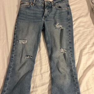 Ljusblå slitna jeans från Junkyard - Ljusblå jeans från Junkyard med snygga slitningar på benen och klassisk femficksdesign. Jeansen har låg midja och är bootcut. Midjemått: 37! Innerbenslängden:81!