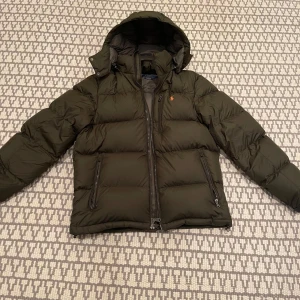 Ralph lauren jacka - Nästan helt oanvänd dunjacka från ralph lauren!! Den är perfekt nu till vintern och har inga deffekter. Den är i Storlek M och är i en snygg grön färg. Vid fler frågor är det bara att kontakta mig