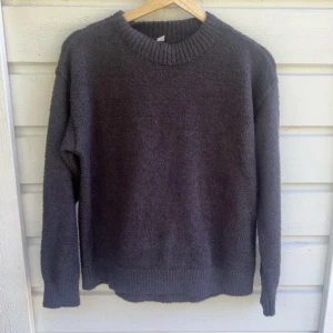 Mörkgrå stickad tröja från Uniqlo - Mysig mörkgrå stickad tröja från Uniqlo i storlek XS. Tröjan har en enkel, rund halsringning och långa ärmar. Materialet är fluffigt och känns riktigt skönt mot huden, perfekt för kyliga dagar. Passformen är normal och ribbade muddar finns vid hals, ärmslut och nederkant.