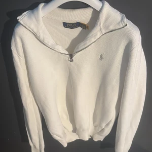 Vit half zip hoodie från Polo Ralph Lauren - Vit hoodie från Polo Ralph Lauren med half zip och broderad logga på bröstet. Tröjan har långärmade ärmar, ribbade muddar och är tillverkad i mjuk bomull. Perfekt för dig som gillar clean och klassisk stil med en sportig touch. Nypris:2200