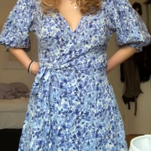 Blommig omlottklänning Gina Tricot - Supersöt omlottklänning från Gina Tricot i storlek 36. Klänningen har blått och vitt blommigt mönster, puffiga korta ärmar och knyt i midjan. V-ringad och lätt, perfekt för varma dagar. Använd 1 gång💕😊