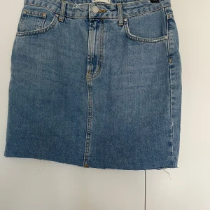 Blå jeanskjol från Gina Tricot - Säljer en klassisk blå jeanskjol från Gina Tricot, modell Perfect Jeans. Kjolen har fem fickor, rå kant nedtill och snygga kontrastsömmar. Passformen är normal och kjolen är kort, perfekt till sneakers eller boots. Jeansmaterialet är slitstarkt och har en cool vintage vibe.