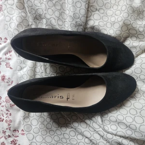 Svarta pumps - Klassiska svarta pumps från Tamaris i mjuk mocka med rund tå och låg klack. Snygg och tidlös modell som passar till många olika outfits. Skorna har en stilren design och är bekväma att bära tack vare den vadderade innersulan. Det är storlek 36 i dem! 🥰