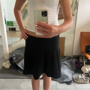 Svart kortkjol med stretchig midja - En svart, enkel och stilren kortkjol med stretchig midja. Kjolen har en lätt utsvängd form som ger en snygg siluett och är gjord i ett mjukt, stickat material. Perfekt att matcha med en croppad topp eller hoodie för en chill look.