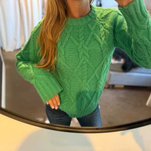 Grön stickad kabeltröja - Snygg grön stickad tröja med grovt kabelstickat mönster och breda muddar vid ärmslut och nederkant. Tröjan har rund halsringning och lång ärm.🍀