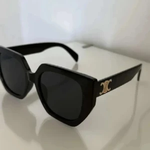 Svarta Céline solglasögon med logga - Snygga svarta solglasögon från Celine med markerad, kantig båge och mörka glas. På skalmen sitter Celines ikoniska guldiga logga som ger en lyxig touch.💕