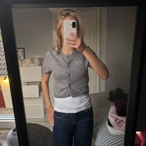 Grå croppad kofta med kort ärm - Grå, croppad kofta med korta ärmar och rund hals. Koftan har knappar framtill och är stickad i ett mjukt material som känns skönt mot huden. 