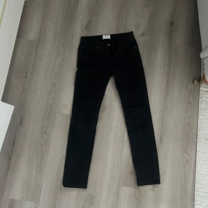 Svarta  jeans från Acne Studios - Svarta jeans från Acne Studios med klassisk femficksdesign och slim fit. Jeansen har hög midja och är tillverkade i ett stretchigt bomullsmaterial som sitter tajt längs benen. Perfekta för dig som gillar en clean och stilren look.
