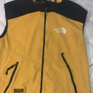 Gul och svart fleeceväst The North Face VINTAGE - Grym gul och svart fleeceväst från The North Face med broderad logga på bröstet. Västen har hel dragkedja framtill, två snedställda fickor med dragkedja och hög krage. Materialet är mjuk fleece och modellen är klassiskt rak.priset kan diskuteras lite vid smidig snabb affär mvh 