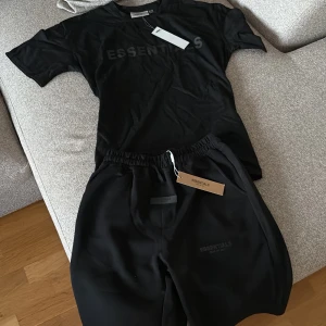 Svart Essentials t-shirt - Svart t-shirt från Essentials med tryckt logga framtill. Klassisk passform med rund hals och korta ärmar. Perfekt för en clean och stilren look. Materialet känns mjukt och skönt mot huden.