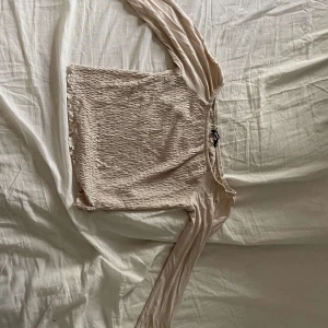 Beige långärmad topp Gina Tricot - Säljer en beige långärmad topp från Gina Tricot i storlek M. Toppen har smockad kropp och raka ärmar i tunt, mjukt material. Den är croppad och har en enkel, stilren look som passar till mycket. Perfekt för dig som gillar neutrala färger och bekväma plagg.