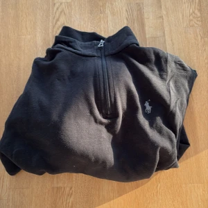 Svart half zip tröja från Polo Ralph Lauren - Svart långärmad tröja från Polo Ralph Lauren med klassisk broderad logga på bröstet. Tröjan har en half zip-dragkedja och hög krage. Mjuk bomullskvalitet som är skön att bära och passar perfekt till lager-på-lager-stil.
