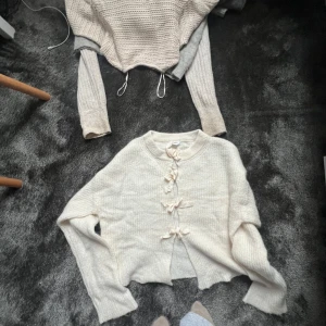  stickad kofta med rosetter - Superfin beige stickad kofta med långa ärmar och söta rosettdetaljer framtill istället för knappar. Koftan har en croppad passform och är perfekt för lager-på-lager. Mjuk och mysig känsla, passar till allt. SKRIV FÖR FLER BILDER 