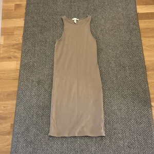 Beige ärmlös klänning från H&M - Säljer en stilren beige klänning från H&M i storlek S. Klänningen är ärmlös med rund hals och har en rak, kroppsnära passform som slutar strax under knäna. Materialet är mjukt och stretchigt, perfekt för en enkel och clean look.