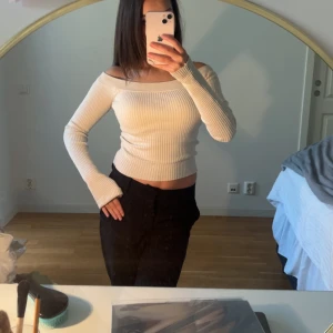 Offshoulder ribbad vit stickad topp - Säljer en superfin offshoulder topp i ribbstickad modell. Toppen är vit, har långa ärmar och sitter tight och croppad över kroppen. Perfekt för dig som gillar en stilren och trendig look med lite edge.