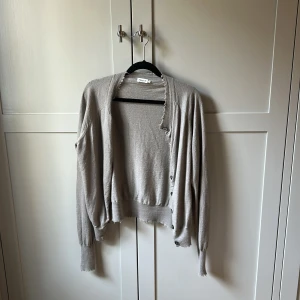 Beige kofta från Filippa K med knappar - Snygg beige kofta från Filippa K i mjuk stickad bomull. Modellen har långa ärmar, knappar framtill och coola råa kanter vid hals och muddar. Perfekt för lager-på-lager och chill stil. Passar dig som gillar minimalistiskt och neutralt.