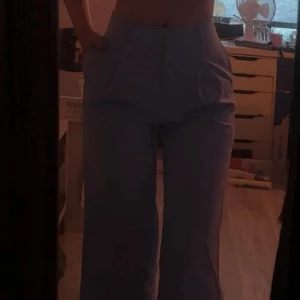 Ljusblå vida kostymbyxor - Säljer ett par ljusblå kostymbyxor med hög midja och vida ben. Byxorna har stora fickor framtill och en clean look utan synliga detaljer. Perfekta om du vill ha en chill men ändå stilren vibe.