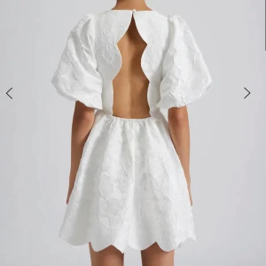 Vit Malina klänning - Superfin vit kort klänning med puffiga korta ärmar och broderat blommönster. Klänningen har en unik öppen rygg med vågiga kanter och elastisk midja. Nederkanten är också vågig för extra detalj. Endast använd en gång så perfekt skick!