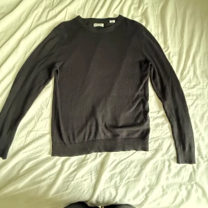 Svart stickad tröja Jack & Jones - En svart stickad tröja från Jack & Jones i storlek S. Tröjan har rund halsringning och långa ärmar, perfekt för lager-på-lager. Enkel och stilren design som funkar till det mesta. Materialet är mjukt och bekvämt.