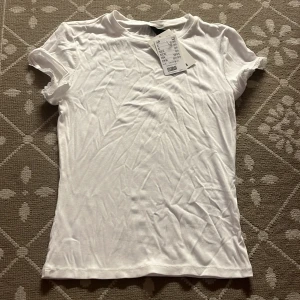 Vit ribbad t-shirt från H&m - Fräsch vit t-shirt från H&m i ribbad bomullsmix. Modellen är kortärmad med rund hals och har en slim passform. Ärmsluten har en liten spetsdetalj som ger en söt touch. Perfekt att styla med jeans eller kjol.