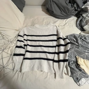 Vit och mörklblå randig stickad tröja från lager 157 - Vit stickad tröja från lager 157 med mörkblåa ränder. Tröjan har en lite högre hals, ribbade muddar och en loose fit. Perfekt för dig som gillar en chill och stilren look. Passar till både jeans och kjol.