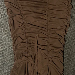 Brun kort omlottklänning från Only - Snygg brun kortklänning från Only med omlottdetalj och rynkade sömmar längs hela klänningen. Modellen är figurnära och har en cool, modern look som passar perfekt för dig som gillar trendiga plagg. Materialet är mjukt och stretchigt polyester.