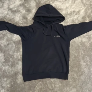 Mörkblå hoodie från A.P.C. - Snygg mörkblå hoodie från A.P.C. med diskret logga och text på bröstet. Tröjan har huva med snörning och långa ärmar, tillverkad i mjuk bomull. Bra skick och priset är inte hugget i sten.
