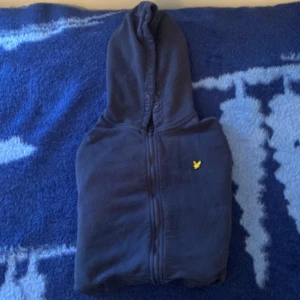 Marinblå hoodie från Lyle & Scott - Säljer en marinblå hoodie från Lyle & Scott med gul broderad fågel på bröstet. Tröjan har dragkedja hela vägen, huva med snörning och två fickor framtill. Perfekt för chill dagar och enkel att matcha med jeans eller joggers. Fick den som en present några månader sen men de va fel storlek och inte använt den alls så mycket sen dess. 