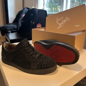 Svarta Christian Louboutin sneakers med nitar - Säljer ett par svarta skor från Christian Louboutin med ikonisk röd sula och nitar på tån. Skorna har snörning och är tillverkade i mocka med detaljer i skinn. Skorna är i storlek 43,5 och säljs nu för de inte passar min stil längre. Skorna är rätt så användna men skriv vid funderingar o mer bilder, och pris kan alltid diskuteras. 