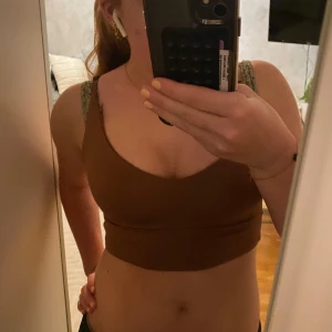 Brun croppad linnetopp - Säljer en brun croppad linnetopp med smala axelband och v-ringning. Toppen har en enkel och stilren design som är lätt att matcha med olika outfits. Perfekt för dig som gillar en clean och trendig look.