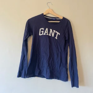 Gant-tröja  - Långärmad tröja från GANT i marinblå färg, storlek XS. Vänligen notera att den har ett litet hål på baksidan, men som är knappt synlig när tröjan sitter på. Material: 100% bomull   Kommer från djur och rökfritt hem. Kan behöva strykas och tvättas då den legat på vinden.  Finns att hämta i centrala Göteborg, eller kan skickas via valfri app. 40kr. 