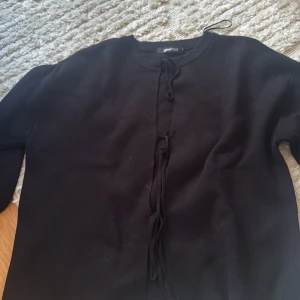 Svart kofta med snörning från Gina Tricot - Svart kofta från Gina Tricot i storlek XS. Tröjan har rund halsringning och snygg snörning framtill som ger en cool touch. Stickad i mjukt material med långa ärmar, perfekt för lager-på-lager under höst och vinter.