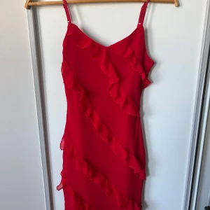 Röd klänning med volanger - Snygg röd klänning med volanger i ett diagonalt mönster. Axelbandslös design som ger en elegant look. Perfekt för festliga tillfällen.