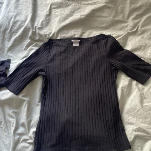 Svart ribbad topp - Säljer en stilren svart ribbad topp med trekvartsärm. Perfekt för en enkel och elegant look. Toppen har en bekväm passform och är lätt att matcha med olika outfits.