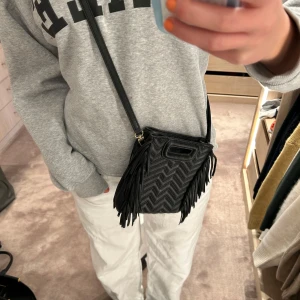 Svart axelväska med fransar - Jättecool och unik maje väska med svart axelband! Köpt för ca 2 år sen men är i bra skick. Vid ”handtaget” har loggan suddats ut men annars inga defekter! Köpt för ca 2000 kr och säljer nu för 1200. Skriv för frågor💘💘