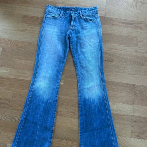 Lågmidjade bootcut jeans - Säljer ett par snygga blå bootcut jeans med slitna detaljer vid fållen från 7 for all mankind. Den har den snyggaste passformen och färgen och är äkta vintage🥹