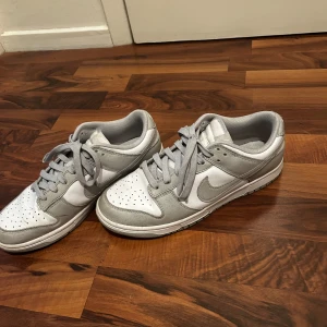 Grå och vita sneakers från Nike - Säljer ett par stilrena grå och vita Nike sneakers med snörning. Skorna har en klassisk design med rund tå och är perfekta för vardagsbruk. De är tillverkade i syntetmaterial och har en bekväm passform.