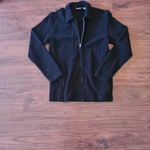 Svart tröja - Snygg svart tröja från Weekday med dragkedja framtill och randigt stickad, manchester. Jackan har en klassisk krage. 